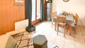 Ein gemütliches Wohnzimmer mit Holzwand, einem Essbereich mit Tisch und Stühlen, einem Kühlschrank und einer Wanduhr.