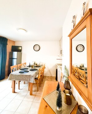 A compact kitchen with a dining area, a refrigerator, a television, and two wall clocks. - Chalet Joue du loup - 6/7 pers (Le Dévoluy)
