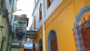 A narrow street with a yellow building featuring a blue sign for a guest house. - SHAW GUEST HOUSE (Kolkata)