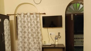 A bathroom with a shower curtain, a mounted television, and a small table with a bottle and a phone. - SHAW GUEST HOUSE (Kolkata)