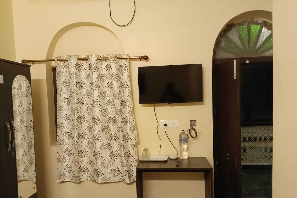 A bathroom with a shower curtain, a mounted television, and a small table with a bottle and a phone.
