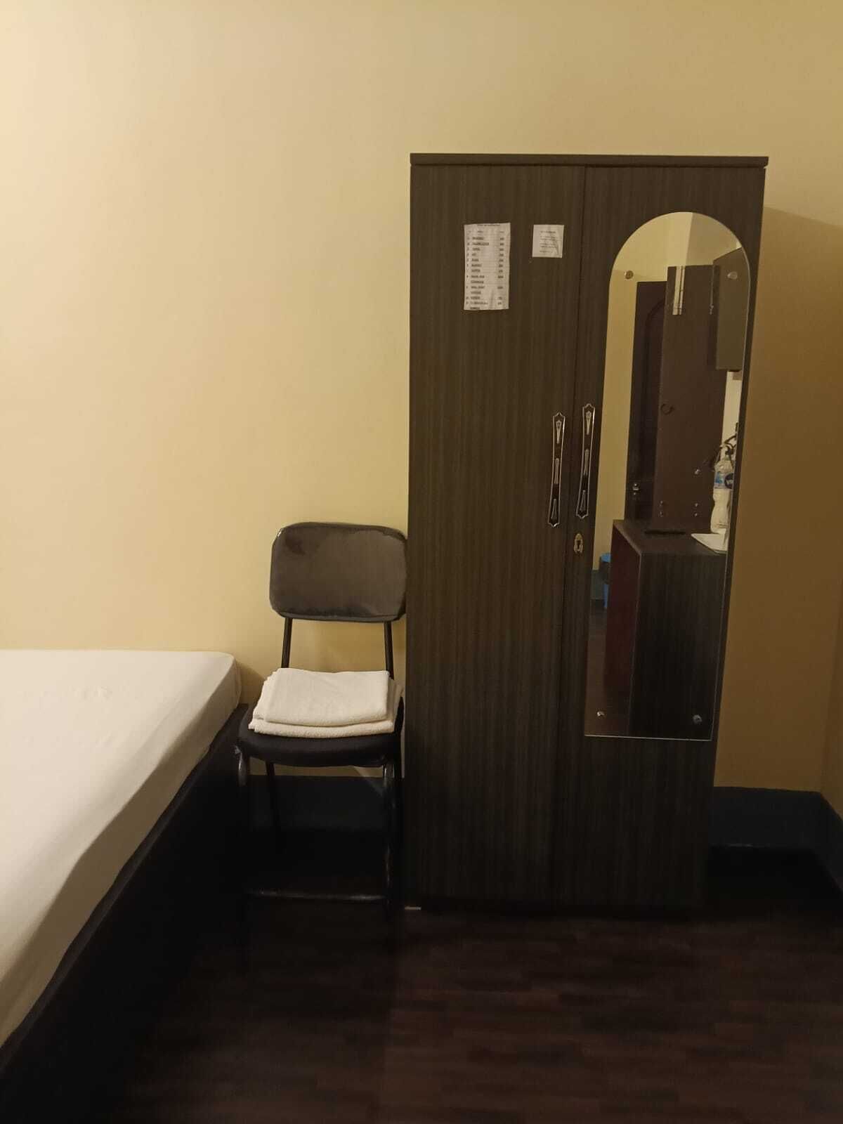 Um quarto pequeno com uma cama de solteiro, um guarda-roupa de madeira com espelho e uma cadeira.