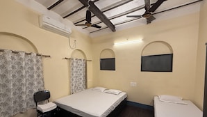 A room with two single beds, a chair, and an air conditioning unit. - SHAW GUEST HOUSE (Kolkata)