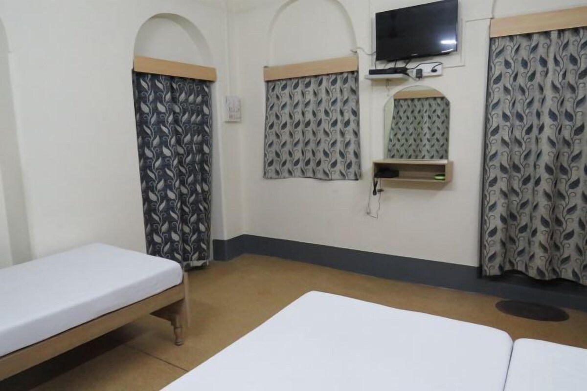 A room with two beds, a television mounted on the wall, and patterned curtains.