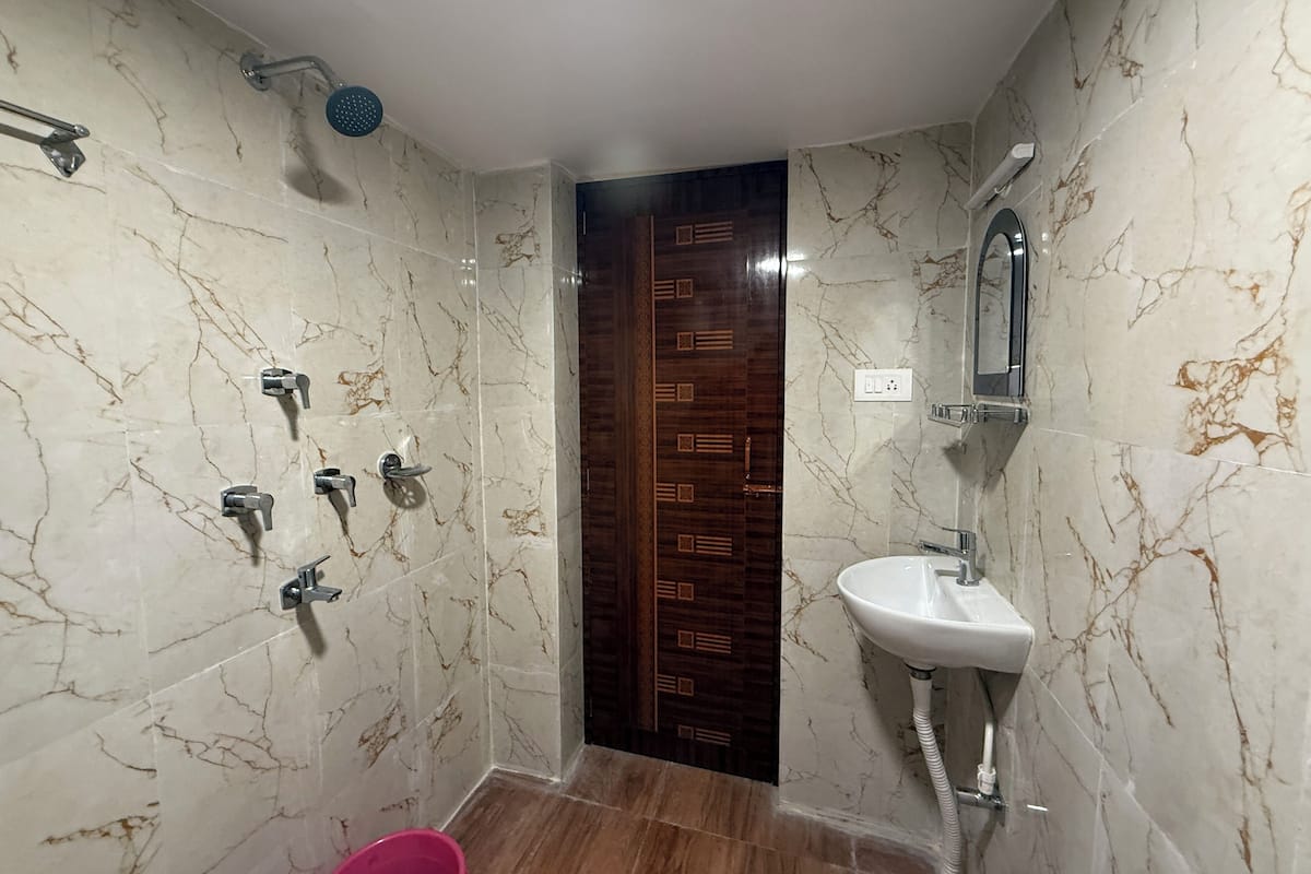 A bathroom with marble walls, a wooden door, a shower, and a sink.
