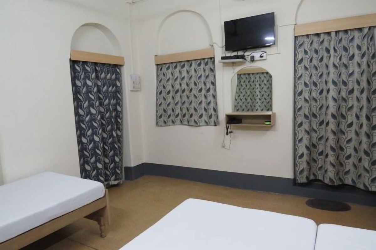 A hotel room with two beds, a TV mounted on the wall, and patterned curtains.