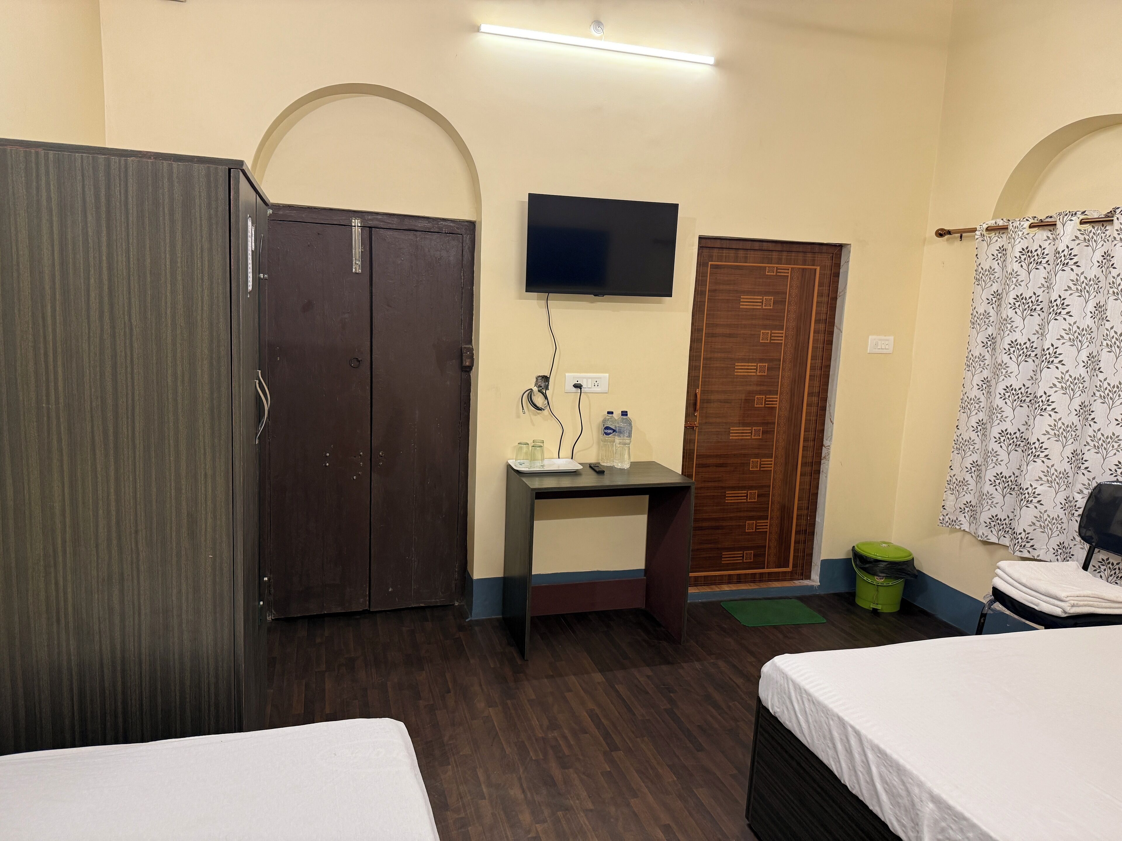 A hotel room with two beds, a desk with a flat-screen TV, a wardrobe, and a bathroom with a shower curtain.
