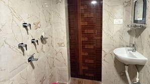 A bathroom with a marble floor, a wooden door, a sink, a mirror, and a shower with a handheld showerhead. - SHAW GUEST HOUSE (Kolkata)