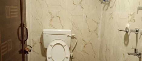 Un baño con inodoro, calentador de agua, ducha y un cubo rosa.