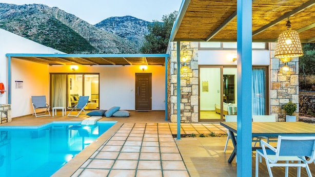 A modern villa with a swimming pool, stone walls, and a view of mountains.