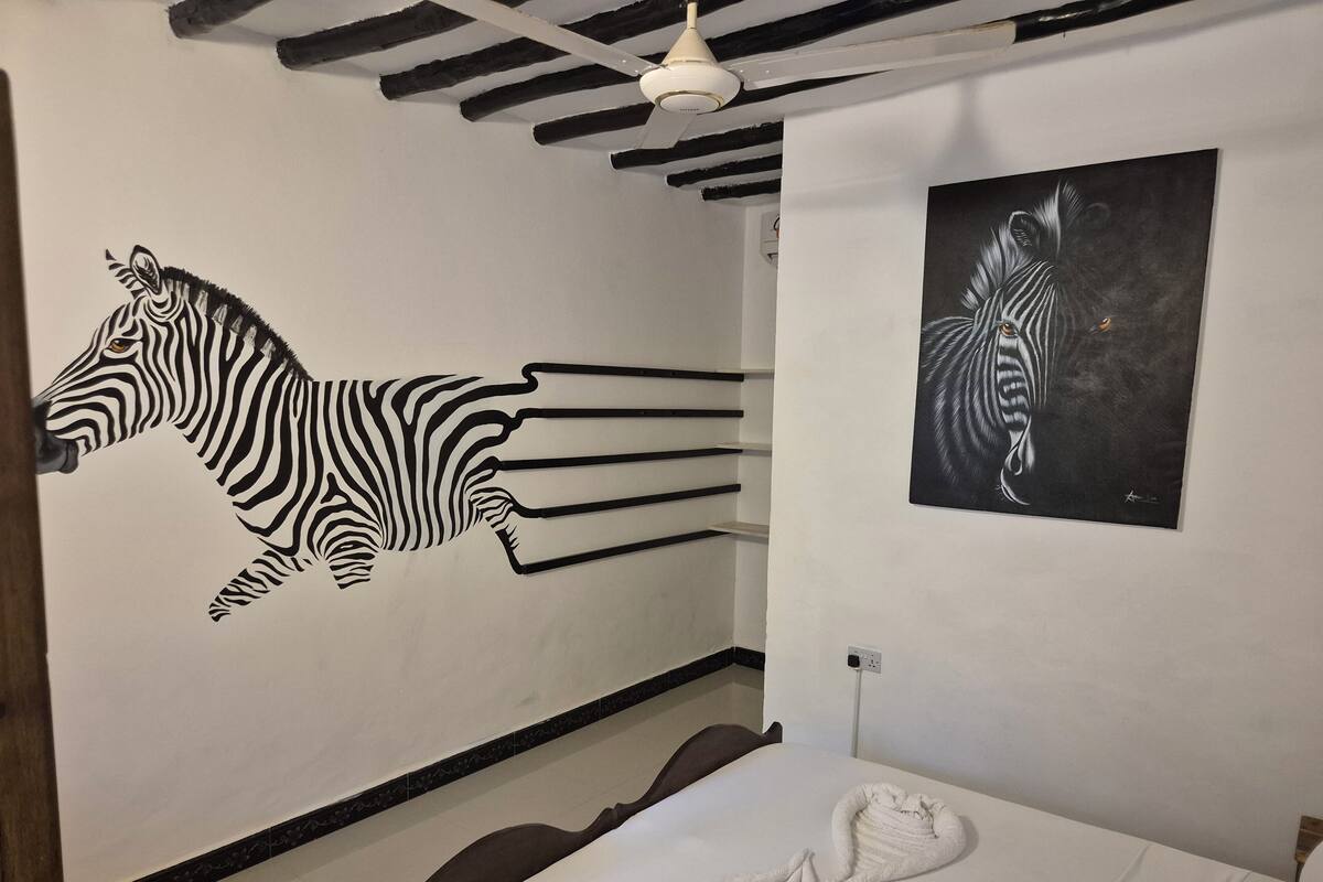 Habitació amb un mural de zebra, un quadre de zebra i un llit amb tovalloles.