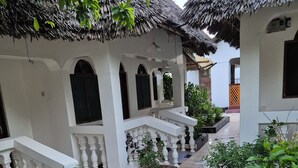 A courtyard with thatched-roof buildings, a tiled pathway, and potted plants. - Ellavita Cottages (Nungwi)