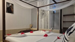 A neatly made bed with white linens and red flowers, a zebra-striped wall, and a painting on the wall. - Ellavita Cottages (Nungwi)