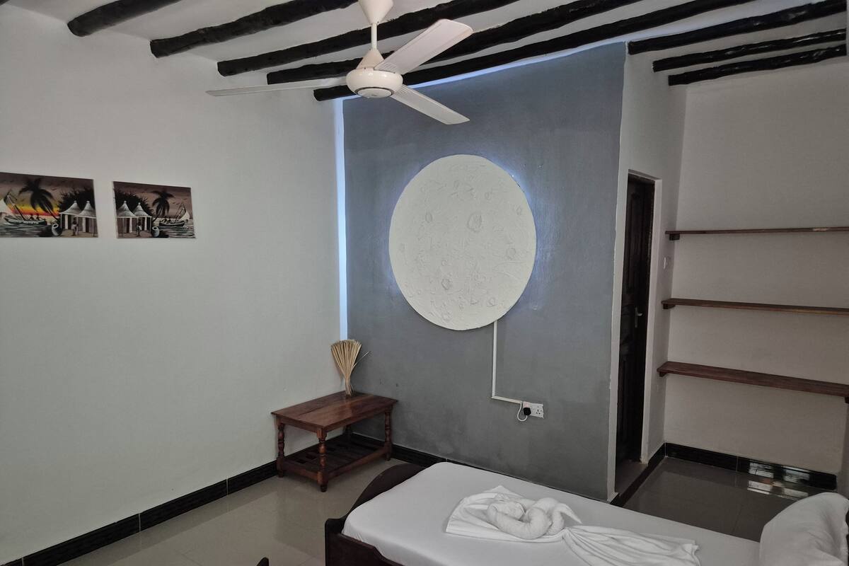 Habitació d'hotel moderna amb un llit, una taula petita, un ventilador de sostre i obra d'art a la paret.