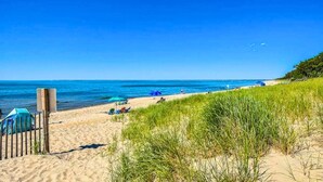 A beach with a wooden fence, a sandy shore, and a grassy dune. - 5-Bedroom Vacation Haven with Pool! (Brewster)
