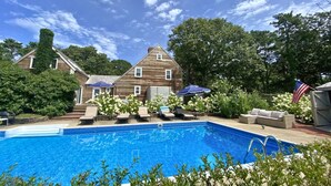 A wooden house with a swimming pool, outdoor furniture, and an American flag. - 5-Bedroom Vacation Haven with Pool! (Brewster)