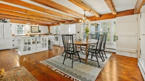 A spacious kitchen with wooden beams, a dining area with a round table and chairs, and a view of the outdoors through large windows. - 5-Bedroom Vacation Haven with Pool! (Brewster)