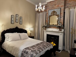 Une chambre avec un grand lit, un lustre, une cheminée et des tableaux encadrés accrochés au mur.