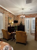 A room with a brick wall, a fireplace, a television, two armchairs, a table, and a chandelier.