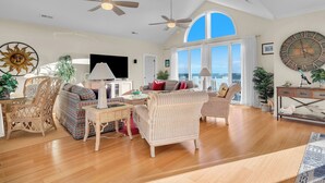 A spacious living room with high ceilings, large windows, and ceiling fans. - One More Day Caswell: Oceanfront Home With Elevator (Oak Island)
