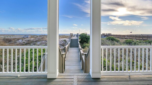 A wooden deck leading to a beach with a white railing, a clear sky, and distant dunes. - One More Day Caswell: Oceanfront Home With Elevator (Oak Island)