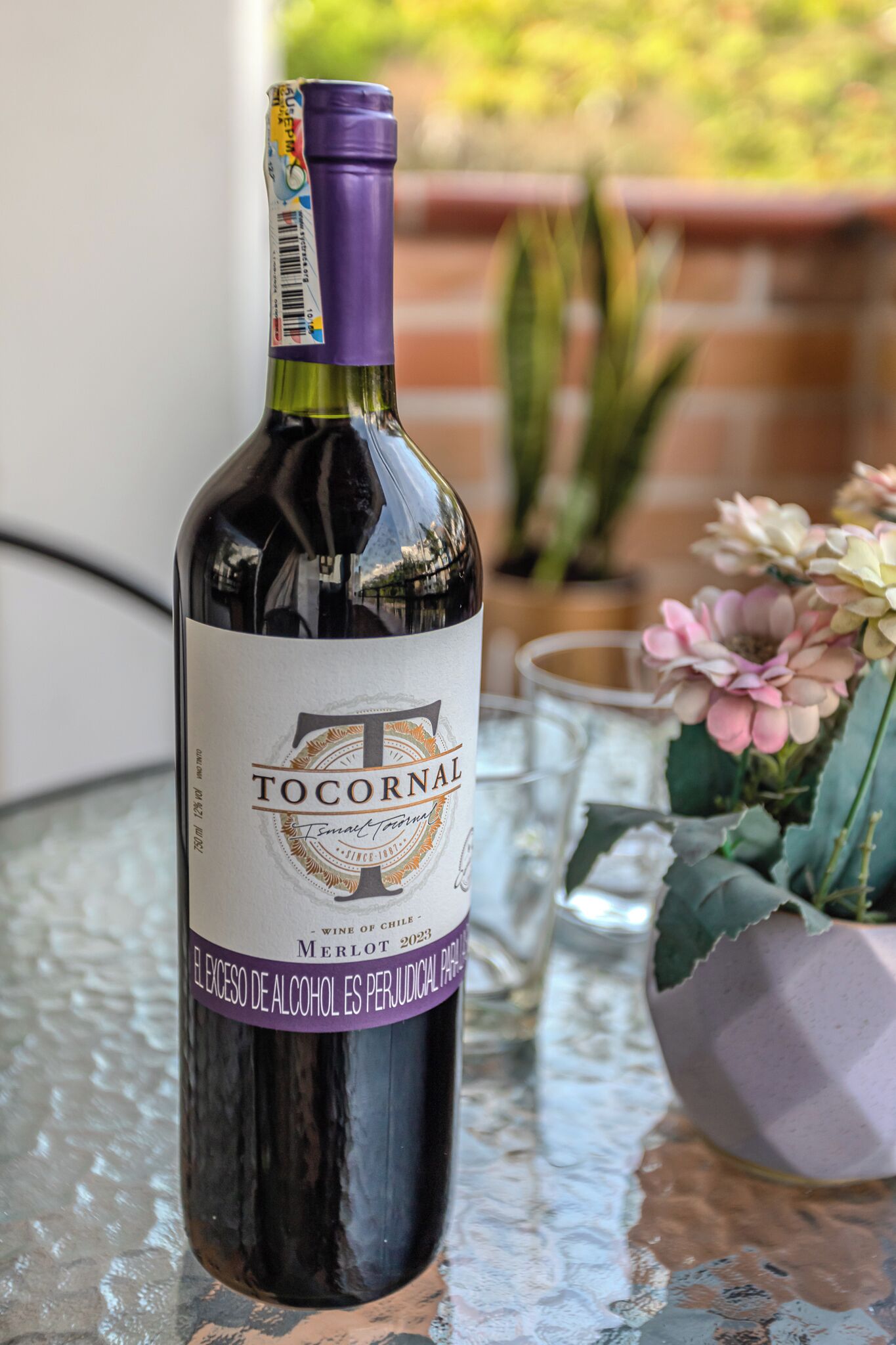 A bottle of Tocornal wine on a table with a glass and flowers in the background.