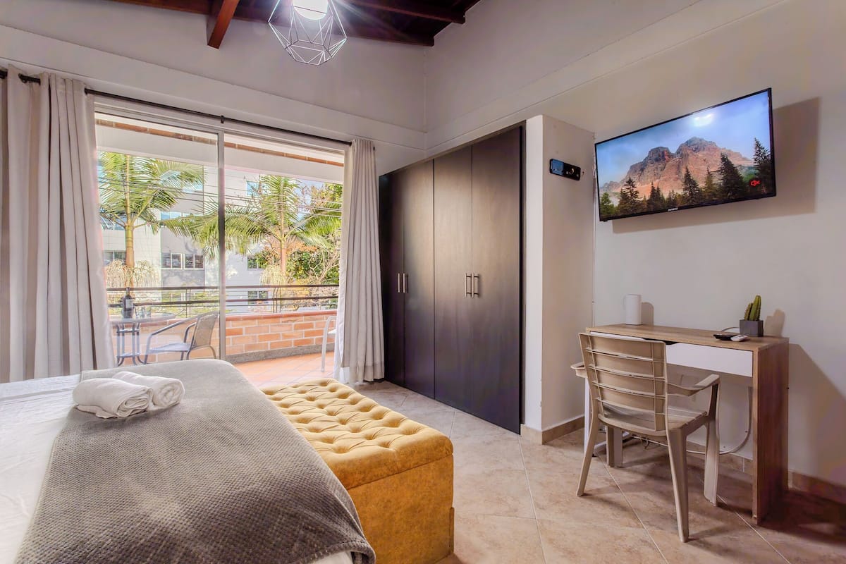 A hotel room with a bed, a desk, a chair, a television, and a sliding door to a balcony.