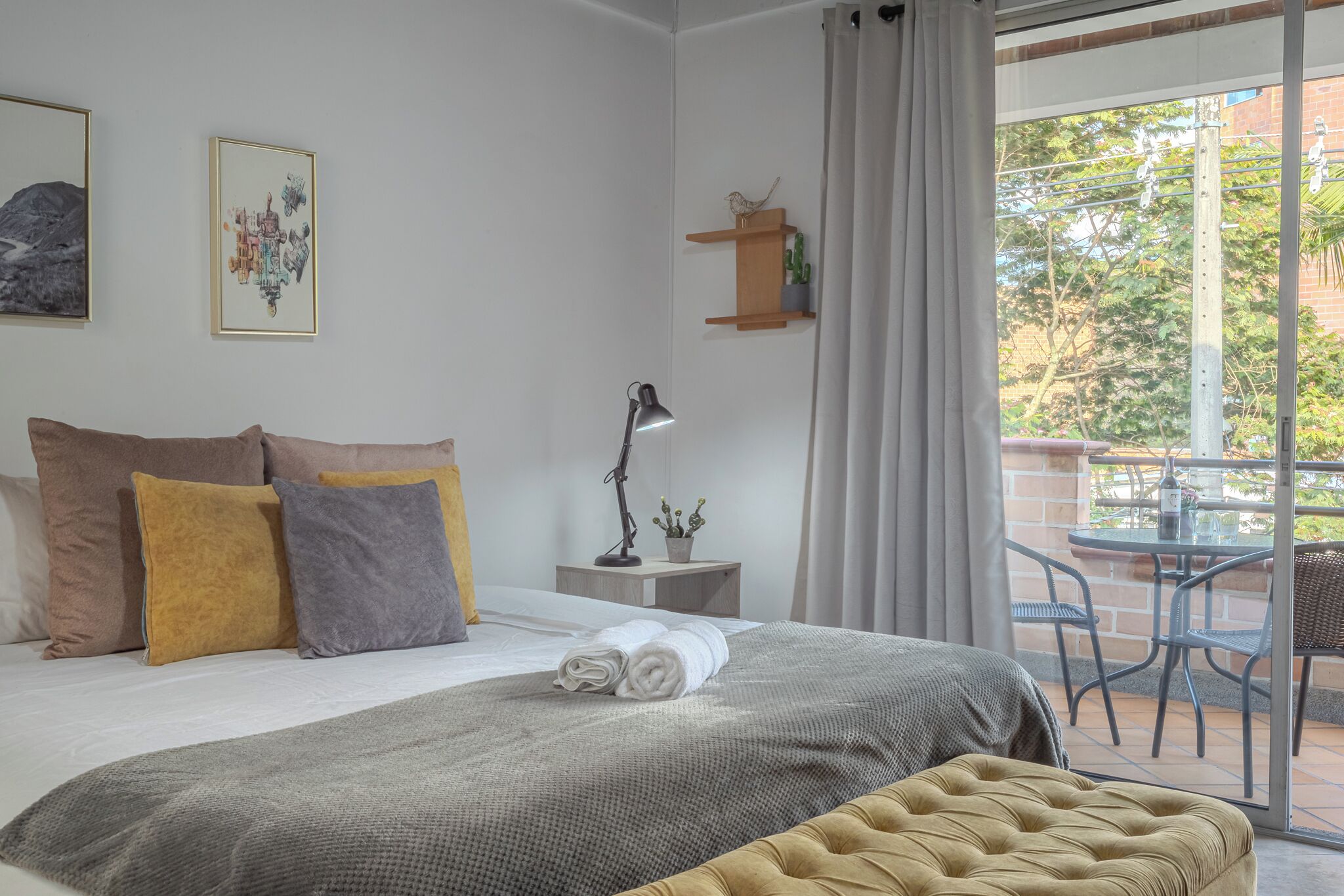 Ein Schlafzimmer mit Bett, Kissen, einem Nachttisch mit Lampe, einer kleinen Ablagefläche mit Pflanzen und Blick ins Freie durch eine Schiebetür.