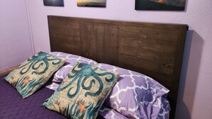 A bed with a wooden headboard, two decorative pillows, and three framed pictures on the wall. - Budget Downtown Studio-G w/Queen Bed,  Micro-Kitchen AC, WIFI & 4 free Streamers (Wailuku)
