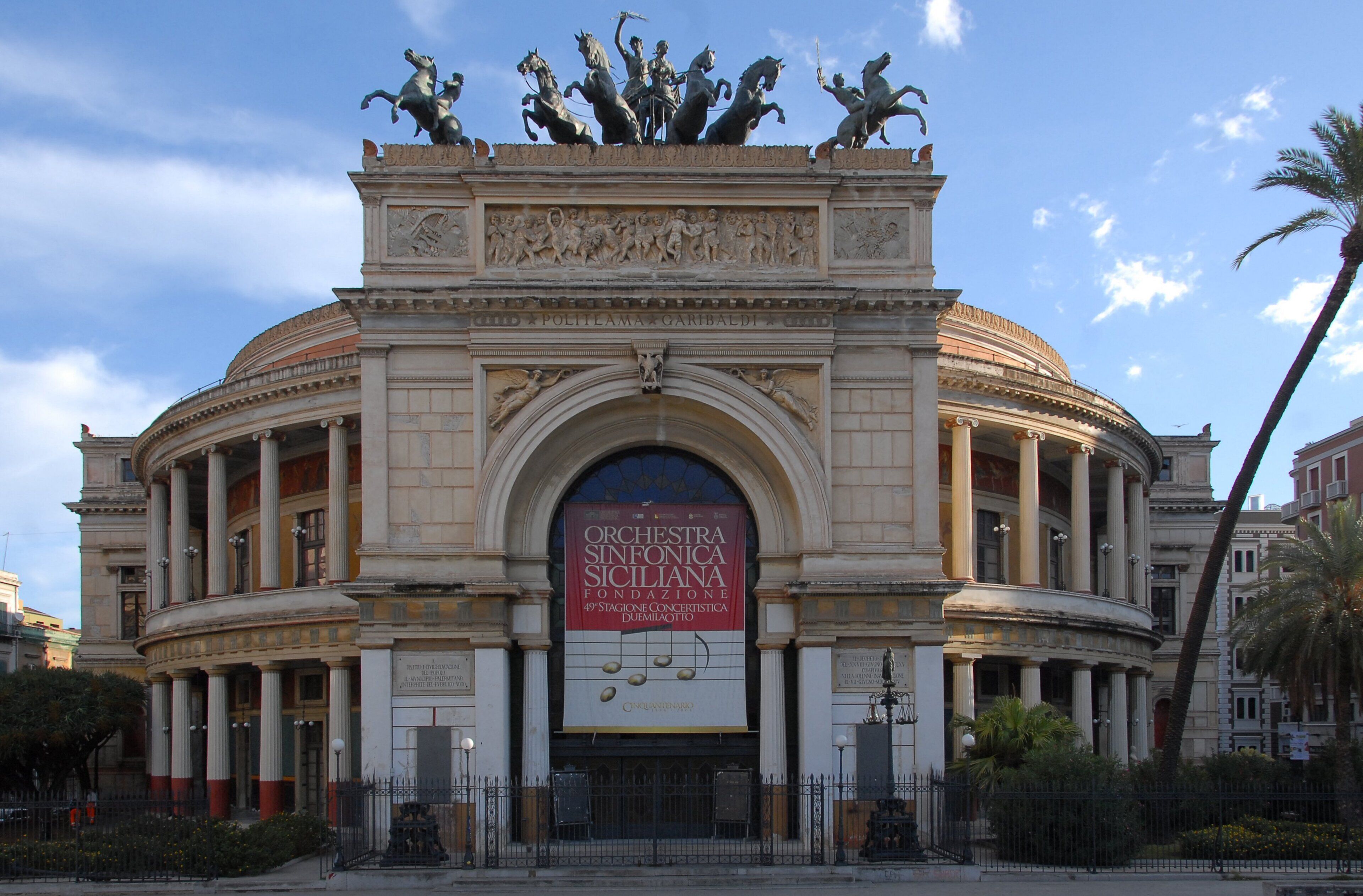 A classical building with an ornate facade, columns, and a large banner advertising an orchestra.