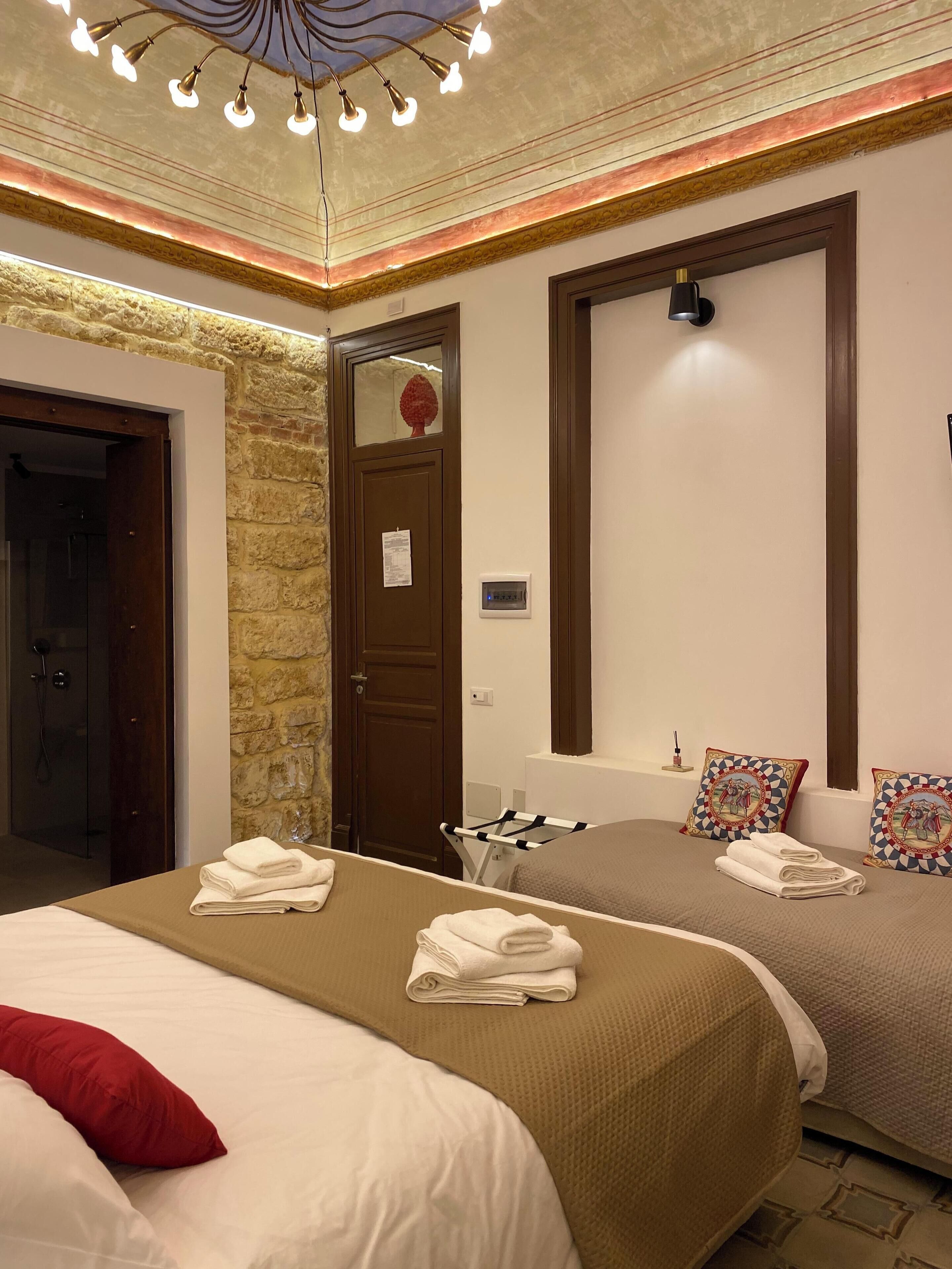 A hotel room with two beds, a stone wall, a wooden door, and a ceiling light fixture.