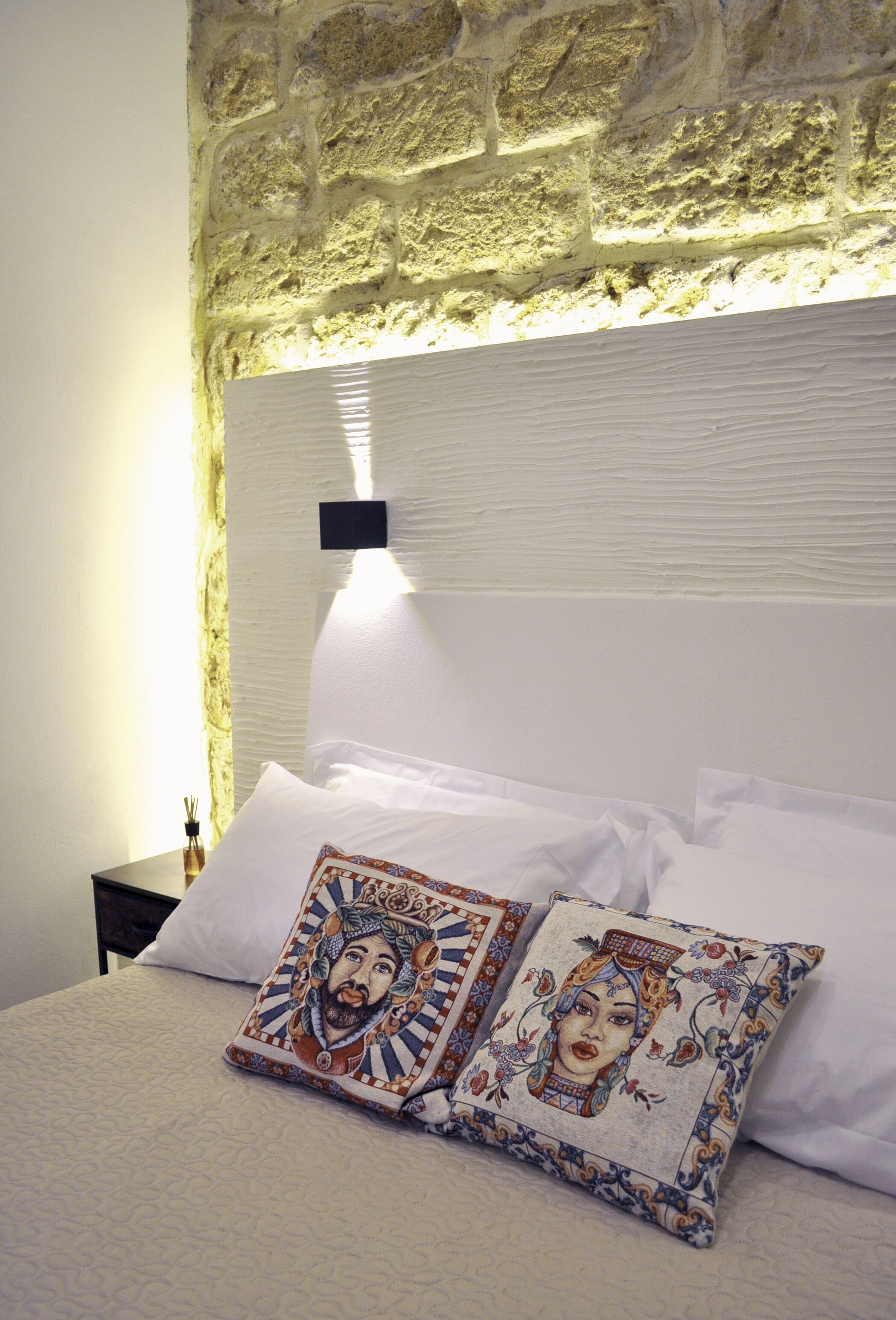 A bed with white linens and two decorative pillows with intricate designs.