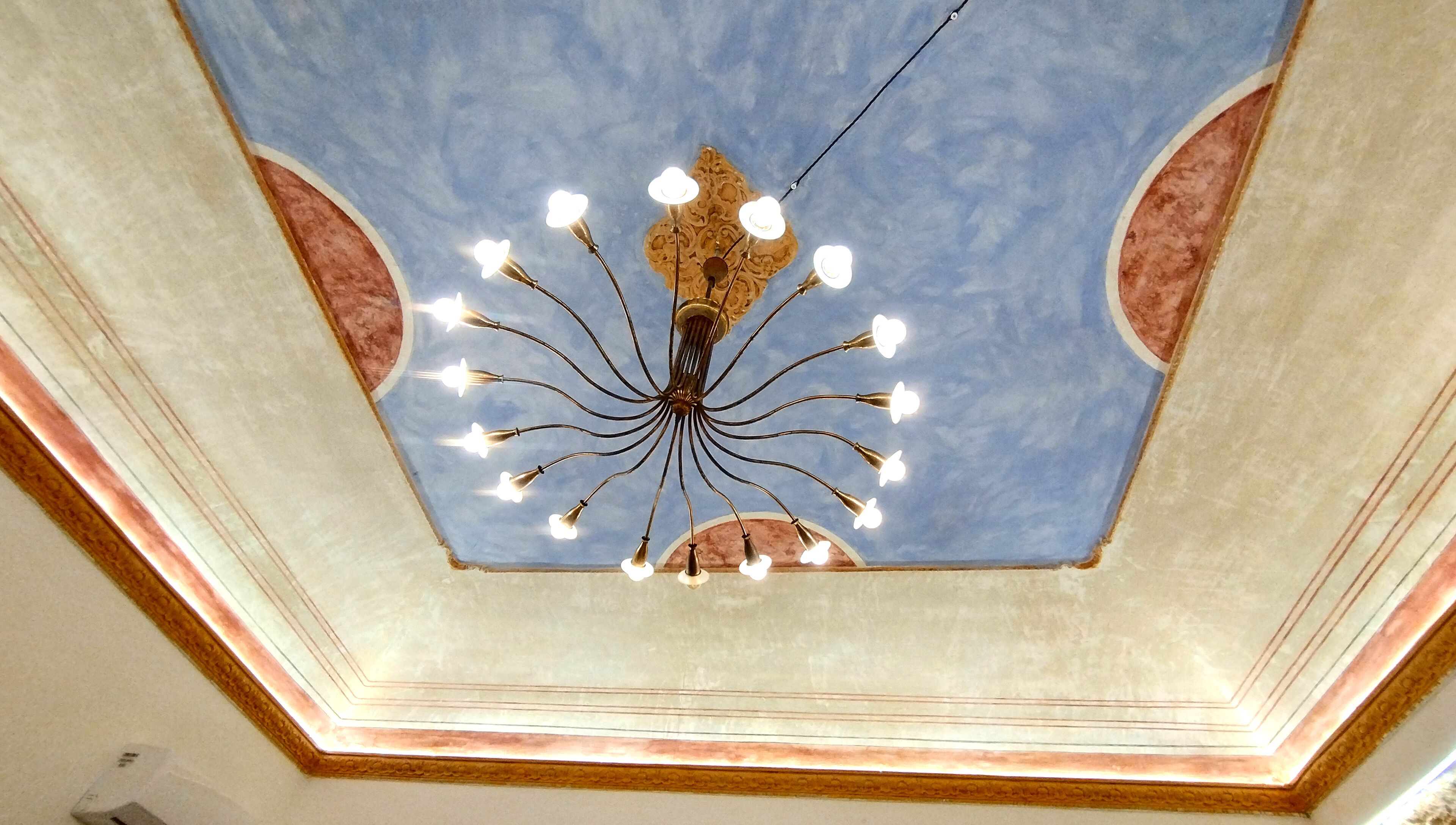 Un plafond orné d’un lustre central et de moulures décoratives.