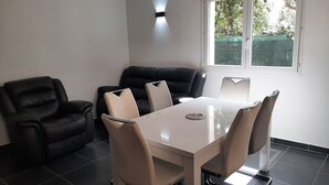 A modern dining area with a white table and chairs, a black leather sofa, and a window with a view of greenery. - Verdon region, house with terrace and garden, 3 bdrms, discount/2nd week (Régusse)