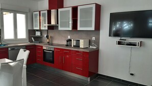 A modern kitchen with red cabinets, a built-in oven, microwave, and a flat-screen TV mounted on the wall. - Verdon region, house with terrace and garden, 3 bdrms, discount/2nd week (Régusse)