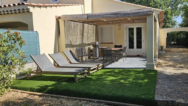 A covered outdoor seating area with lounge chairs and a table, a door, and a small garden with artificial grass. - Verdon region, house with terrace and garden, 3 bdrms, discount/2nd week (Régusse)