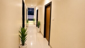 A hotel hallway with a view of the night sky through a window, potted plants, and a door with a sign. - Hotel Shivaay  (Indore)