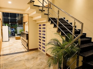 A modern interior with a staircase, a refrigerator, a wooden cabinet, and a potted plant. - Hotel Shivaay  (Indore)