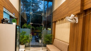 A modern interior with a sofa, a fan, a glass door leading outside, and a small table. - Hotel Shivaay  (Indore)