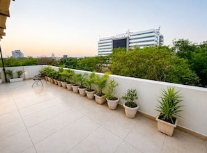 Terraza en la azotea con plantas en macetas, una silla y vistas de la ciudad.