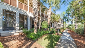 A pathway flanked by palm trees and a building with large windows and a balcony. - Golf Cart Included, 3 Pools, Steps to Beach, Pickleball (Santa Rosa Beach)