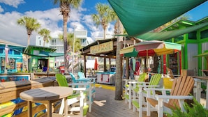 A wooden deck with outdoor seating, palm trees, and a sign reading "Artists at Gulf Place". - Golf Cart Included, 3 Pools, Steps to Beach, Pickleball (Santa Rosa Beach)