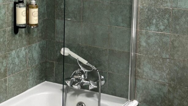 A bathroom with a bathtub, a shower, and a wall-mounted sink. There are two bottles of shampoo and conditioner on the wall. - Lam Hotel Fortaleza de Almeida (Almeida)