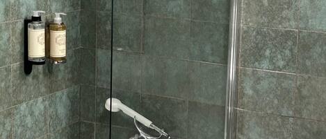 A bathroom with a bathtub, a shower, and a wall-mounted sink. There are two bottles of shampoo and conditioner on the wall.