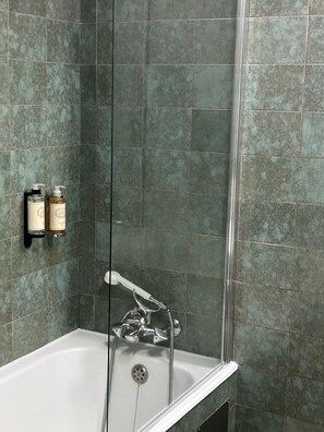 Ein Badezimmer mit Badewanne, Dusche und einem wandmontierten Waschbecken. An der Wand befinden sich zwei Flaschen Shampoo und Conditioner.