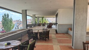 A covered outdoor seating area with tables and chairs, a view of buildings and trees, and a tiled floor. - Lam Hotel Fortaleza de Almeida (Almeida)