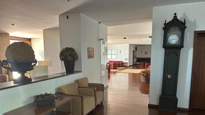 A spacious living room with a wooden floor, a large clock, and a seating area with a table and chairs. - Lam Hotel Fortaleza de Almeida (Almeida)