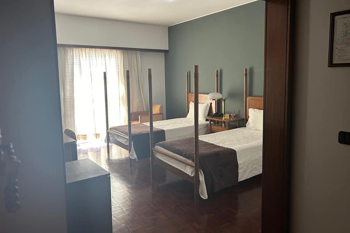 Una habitación de hotel con una cama con dosel, una mesita de noche con lámpara y una silla.