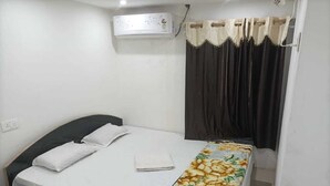 A single bed with a white mattress, a floral bedspread, and a dark headboard. An air conditioning unit is mounted on the wall above the bed. - Hotel Dharam Mukti (Raxaul)