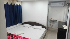 A bedroom with a bed, a bedside table, a small sink, and an air conditioning unit. - Hotel Dharam Mukti (Raxaul)